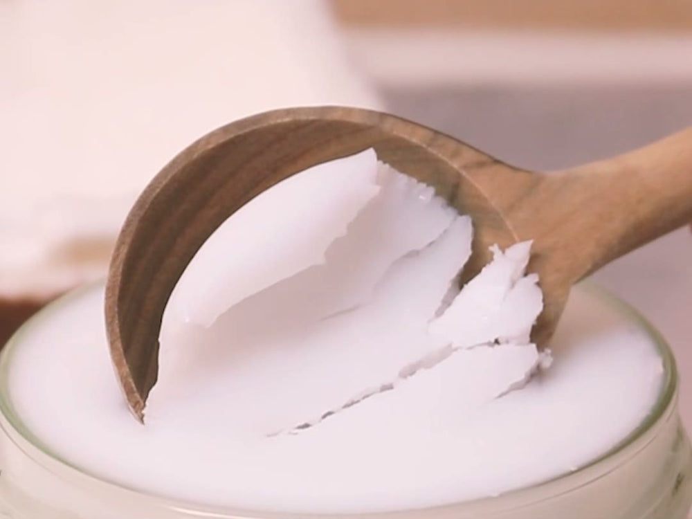 Cuchara de madera sacando aceite de coco sólido del frasco