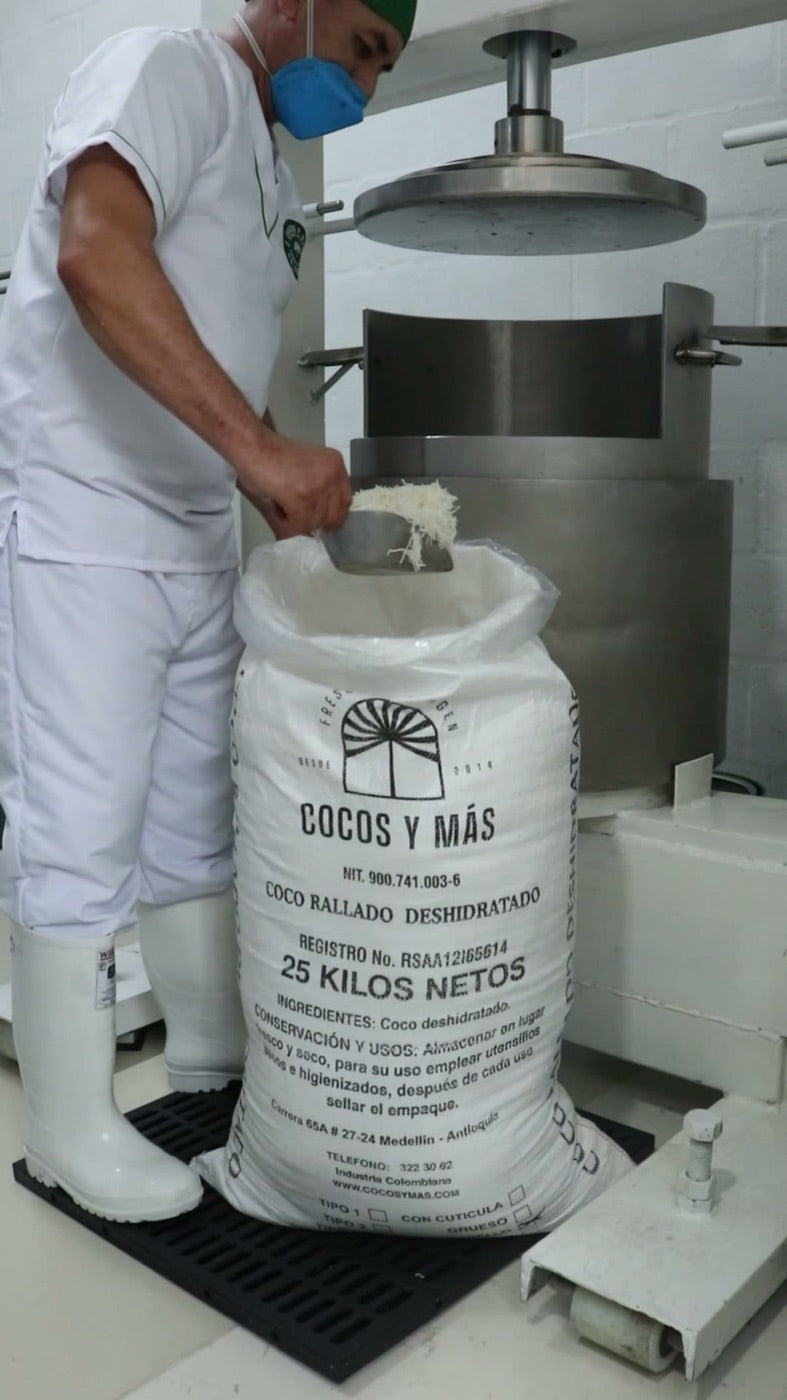 Operario cargando coco rallado deshidratado en la prensa de acero inoxidable de la planta
